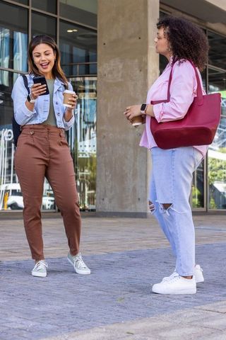 African american women chatting and holding coffee outside modern glass office entrance