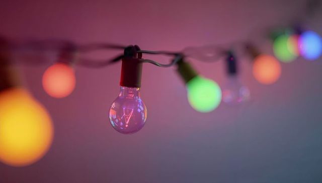 Hanging clear bulb glowing with visible filament and colorful bokeh string lights ambiance decor