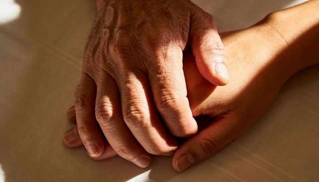 Senior Hand Resting Over Adult Hand in Warm Sunlight Conveying Comfort and Support