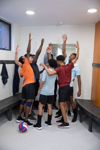Male volleyball team huddling in locker room raising hands celebrating unity and focus