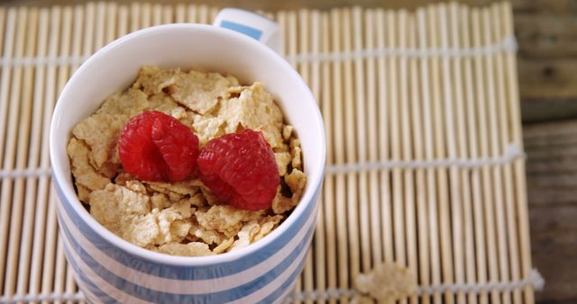 A close-up of a bowl filled with cereal flakes and fresh raspberries on a textured wooden surface. Ideal for use in articles or marketing materials related to health, breakfast recipes, and natural foods. Great for promoting healthy eating, nutritional guides, and organic diet plans.