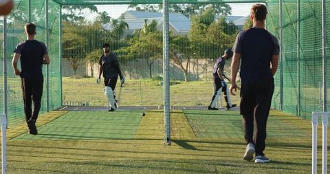 Cricket players practicing in outdoor nets during batting and fielding drills on turf