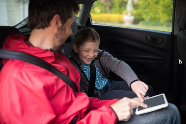 Father and daughter sitting in the back seat of a car, using a digital tablet together. Both are smiling and enjoying their time. Ideal for use in family, technology, travel, and lifestyle contexts, highlighting family bonding, modern parenting, and safe travel.