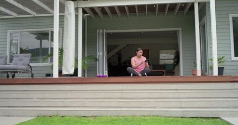 Woman sitting on deck using smartphone with dumbbells nearby during outdoor workout break