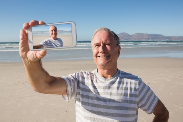 Smiling senior man holding smart phone while standing against sea - Download Free Stock Photos Pikwizard.com