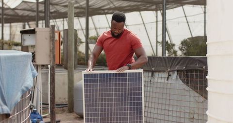 Technician Setting Up Solar Panel in Eco-Friendly Greenhouse
