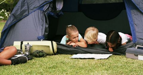 children are leaning in together inside a tent at a campsite, embodying exploration, friendship, and fun. ideal for showcasing outdoor activities, familial bonding, or promoting camping and outdoor lifestyle activities. great for marketing summer camps or youth adventure programs.
