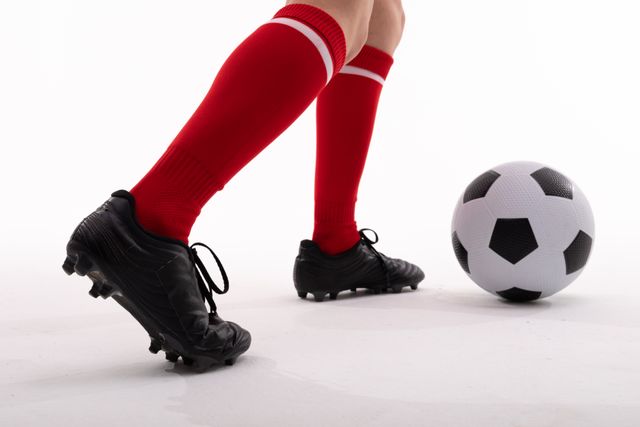 Low section of caucasian female player wearing red socks kicking soccer ball on white background. unaltered, sport, competition and game concept.