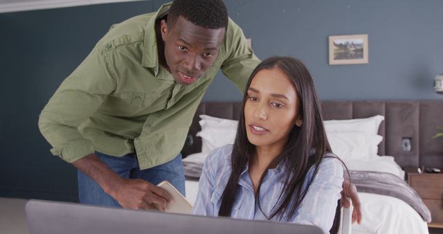 Young couple engaging in online shopping, using a laptop in a cozy bedroom setting. Ideal for illustrating modern lifestyle, e-commerce, technology integration in everyday life, and healthy relationships promoting teamwork and shared activities at home.