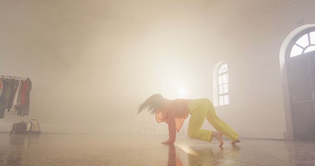 Contemporary dancer bending over and moving expressively in studio with dramatic backlighting. Highlights flexibility, grace, and artistic expression. Ideal for use in articles about dance, fitness, and artistic performances, or in promotional materials for dance studios and workshops.