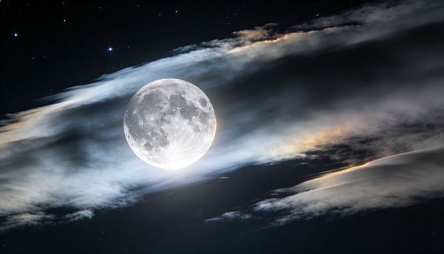 Full moon illuminating thin clouds and starry night sky