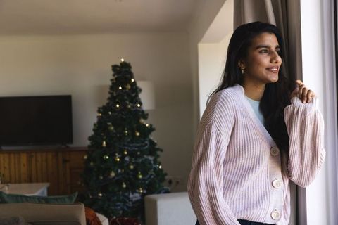 Smiling woman by window with christmas tree in cozy living room