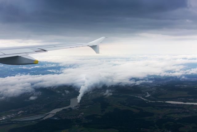 A view from an airplane showing the aircraft wing in the foreground with an expansive sky filled with clouds. Below, a cityscape with industrial areas can be seen with a river winding through the land. This image is ideal for travel blogs, aviation promotions, and tourism websites seeking to illustrate the experience and perspectives of air travel.