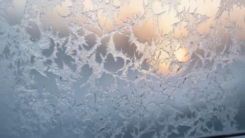 Sliding camera revealing frost-covered window with sunrise glow through ice crystals