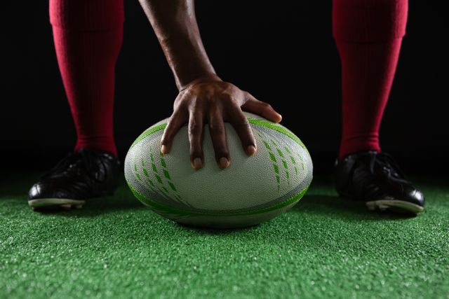 Low section of sportsperson on rugby ball against black background