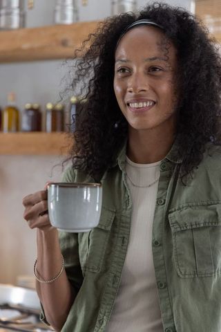 Smiling african american woman holding ceramic mug in rustic kitchen morning comfort