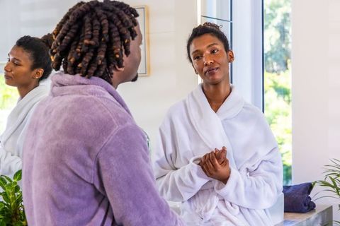 Sunlit morning couple chatting at bathroom vanity wearing robes sharing calm intimate moment