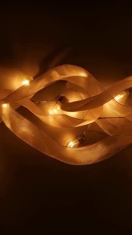 Shifting Mesh Ribbon Lights Settling into S Shape on Dark Table, Glowing Amber Vertical Video