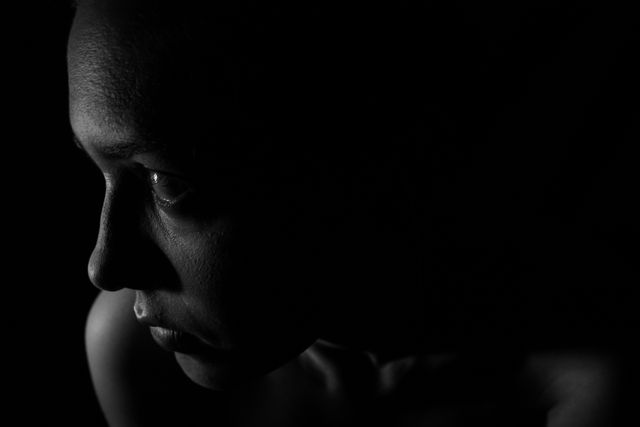 Emotive black and white close-up of woman’s face in shadows, useful for mental health, sadness, loneliness, introspection, or artistic publications.