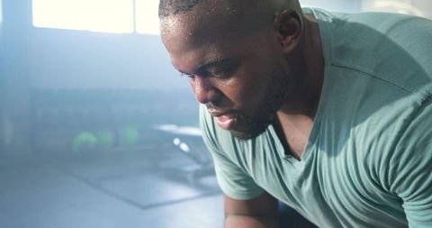Catching breath after intense strength training, man leaning on bench, focused and sweaty