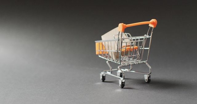 Mini shopping cart holding small box on dark background. Ideal for illustrating concepts related to online shopping, marketing strategies, retail commerce, and e-commerce. Suitable for website banners, marketing campaigns, and online store promotions.