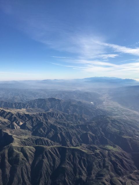 An expansive aerial view captures the rugged mountain landscape with clear blue skies and distant horizons. The image highlights unique patterns of valleys and high-altitude terrain, ideal for use in projects focusing on nature, adventure, or travel. Additionally, this photograph can be featured in environmental documentaries, outdoor adventure blogs, or promotional materials spotlighting scenic beauty and natural attractions.