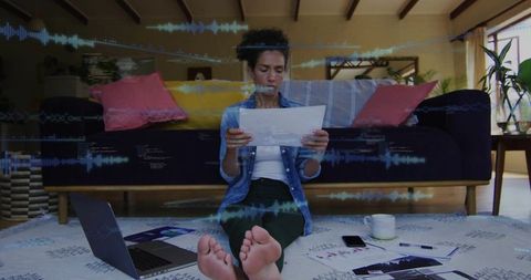 Woman reading financial reports on floor with laptop and data waveform overlay