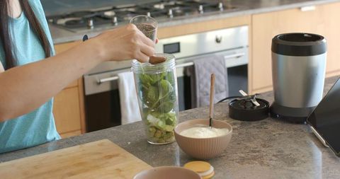 Asian woman preparing green smoothie with chia seeds and yogurt in modern kitchen