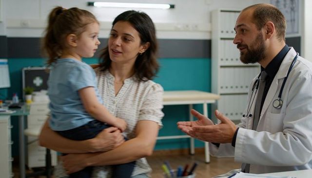 Pediatrician consulting with mother holding toddler during clinic wellness visit