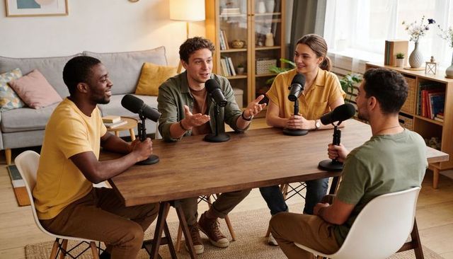 Four hosts recording conversational podcast around wooden table in cozy bright living room