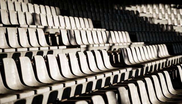 Sunlit empty stadium seats casting dramatic shadows in repeating concrete rows