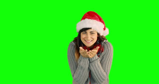 This image features a woman wearing a Santa hat, gray sweater, and scarf smiling and blowing a kiss. The green screen background makes it perfect for holiday-themed advertising, greeting cards, websites, and social media posts. The cheerful and festive expression can enhance promotional materials and celebration messages.