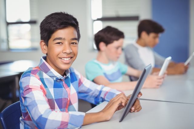 Image shows a smiling student using a digital tablet in a classroom. Other students are focused on their tablets in the background. This image is ideal for educational and technology-related content, showcasing modern learning environments, classroom activities, and student engagement.