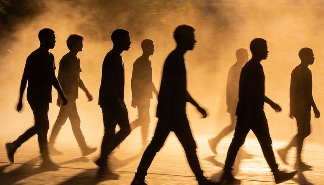 Silhouetted men walking through amber mist at sunset, casting long shadows and cinematic rimlight