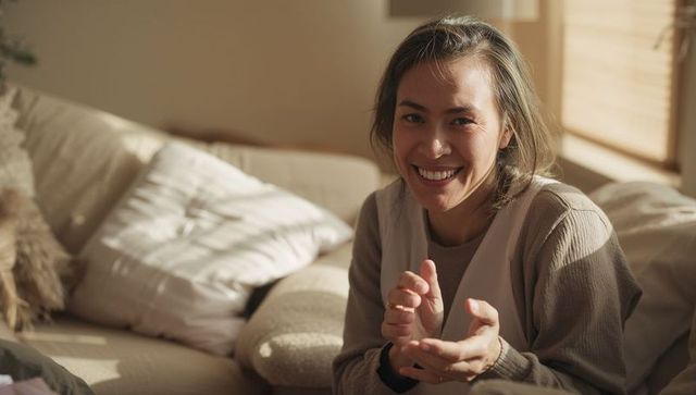 Sunlit woman smiling on cozy beige sofa, sharing warm relaxed moment in living room