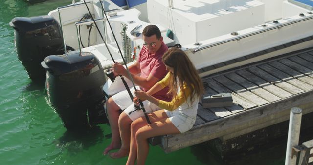 Happy caucasian father teaching teenage daughter fishing, sitting on jetty by boat on a sunny day. Leisure, free time, hobbies, family, travel and vacations.