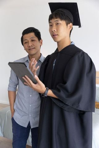 Young asian graduate holding tablet celebrating virtual graduation with proud family