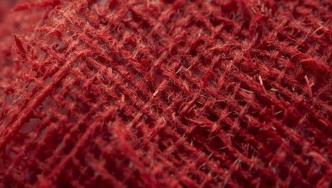 Displaying frayed red burlap weave with coarse fiber texture in tight macro detail