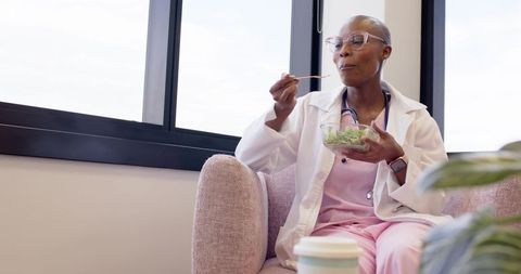Clinician enjoying salad break in lounge wearing pink scrubs and white coat