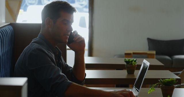 Businessman talking on phone and using laptop in modern cafe. Ideal for concepts of remote work, business communication, technology use, and professional environments. Can be used in business websites, tech blogs, and promotional materials.