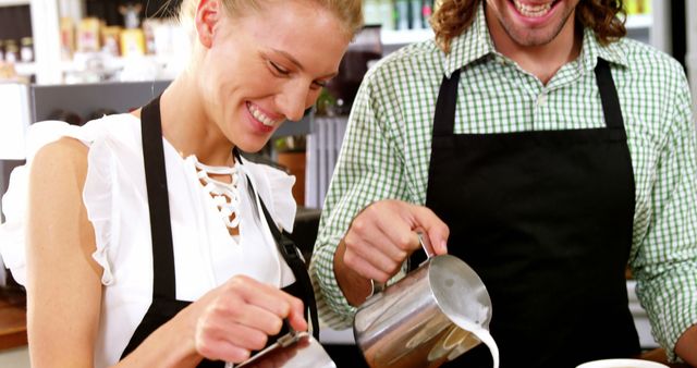 This image shows two baristas working together in a bright, lively cafe, pouring milk into coffee cups. Ideal for use in blogs or articles about cafe culture, barista training, or teamwork in hospitality settings. It emphasizes collaboration, professional service, and enjoyment of work, making it suitable for marketing materials for cafes or coffee shops.