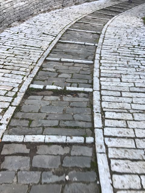This image depicts a curved stone pathway bordered by an orderly arrangement of white bricks. Ideal for use in travel blogs, historical sites promotions, urban architecture guides, or as background in projects emphasizing rustic and historical themes.