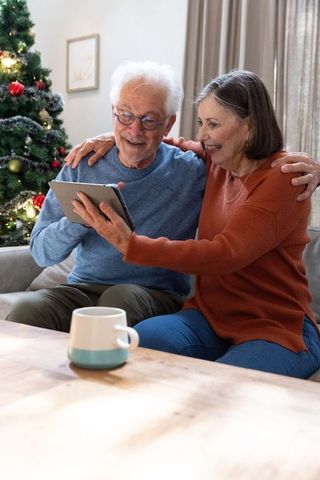 Senior Couple Enjoying Tablet Near Christmas Tree