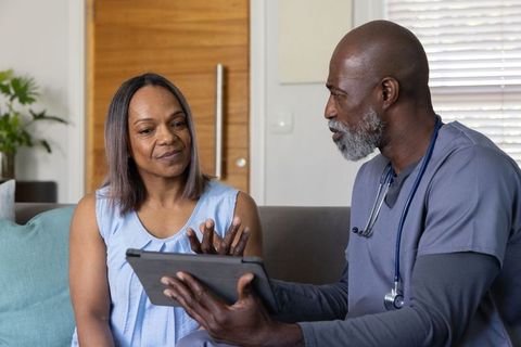 Clinician conducting at-home tablet consultation with patient on living room sofa