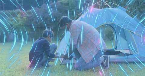 Father and son assembling tent on grass with neon light trails, family camping bonding