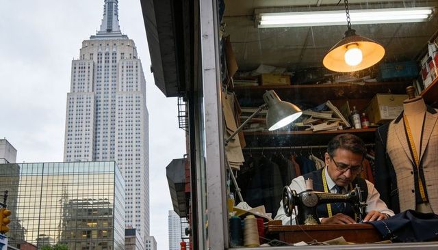 Urban tailor stitching bespoke suit beside city skyline and vintage sewing machine window