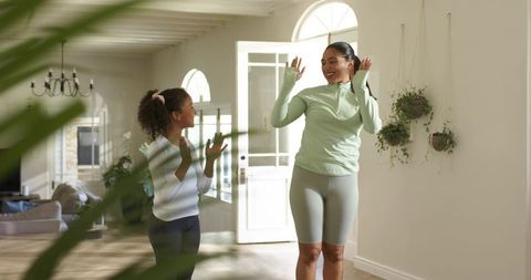 Mother and daughter celebrating in activewear at sunlit home entryway
