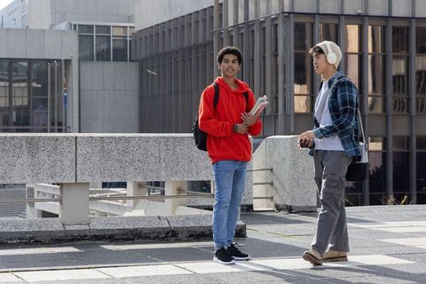 Multicultural teens talking on urban campus plaza holding backpacks and notebooks