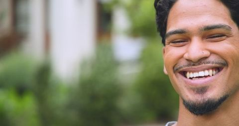 Smiling Young Man Outdoors in Casual Attire Among Greenery