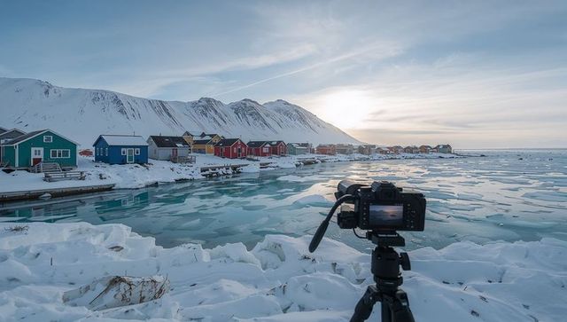 Dslr on tripod capturing colorful coastal cabins beside frozen arctic bay at sunrise